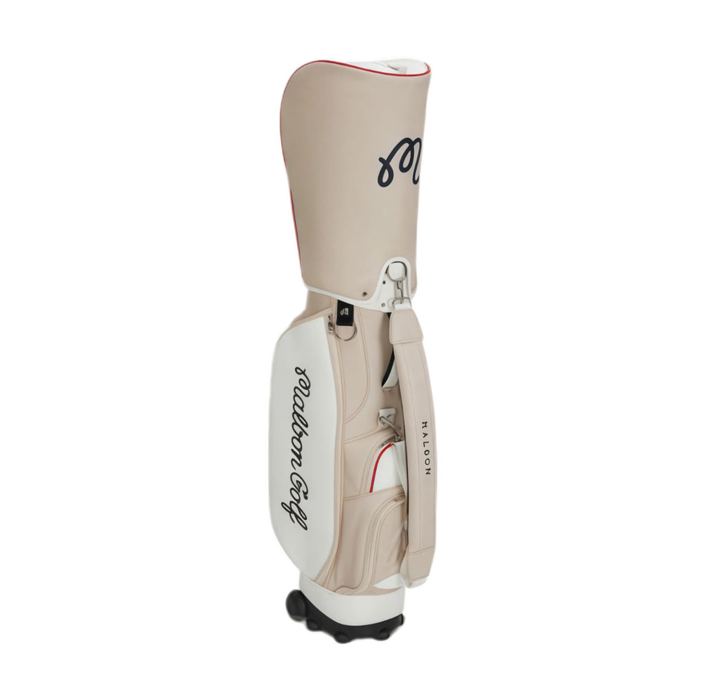 Rear view of beige Malbon Golf cart bag showcasing "Malbon Golf" script logo, padded shoulder strap, and Halon-branded handle. Designed for comfort and style during play.