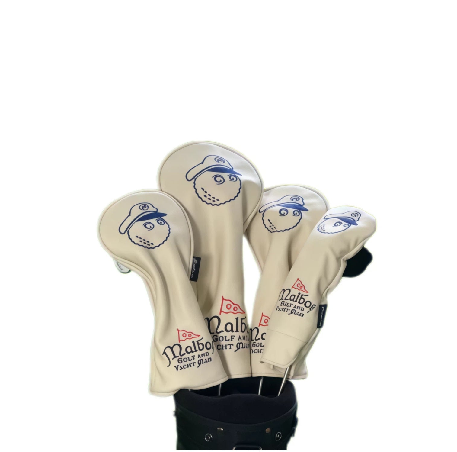 Cream beige Malbon golf headcovers displaying navy blue cartoon captain face and red flag logo, neatly covering golf clubs in a premium black golf bag.