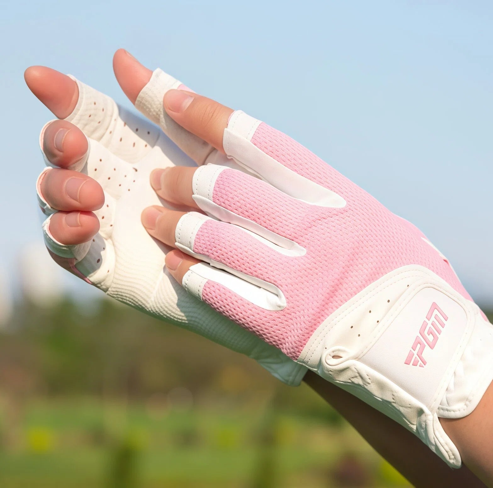 A detailed view of the back of a pink PGM women's fingerless golf glove. The image showcases the breathable mesh fabric, the stylish finger design, and the prominent PGM logo on the wrist strap.