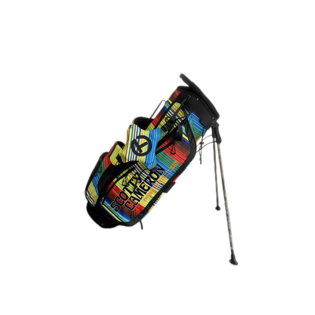 An angled view of the Scotty Cameron Junior Serape Circle T Stand Bag. This lightweight golf bag features a vibrant, multi-colored serape stripe pattern in red, yellow, blue, and green, with the iconic black Circle T logo on the pocket.
