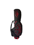 Angled front view of the Scotty Cameron Supercar Staff Bag in black, highlighting the large red "NOV" crown design, multiple storage pockets, and the integrated carry handle with red accents.